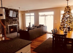 Un salon chaleureux avec une cheminée, un mur en pierre, une grande fenêtre et un sapin de Noël.