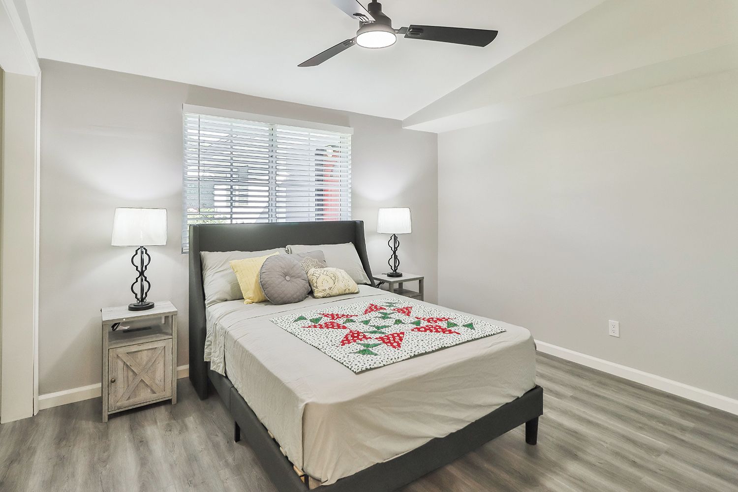 Quarto com uma cama, duas mesas de cabeceira, um ventilador de teto e uma janela com persianas.