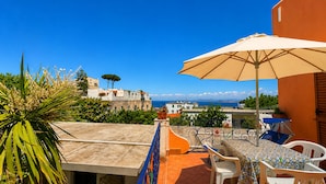 Una terraza con mesa y sillas, una sombrilla grande y vistas al mar y edificios.