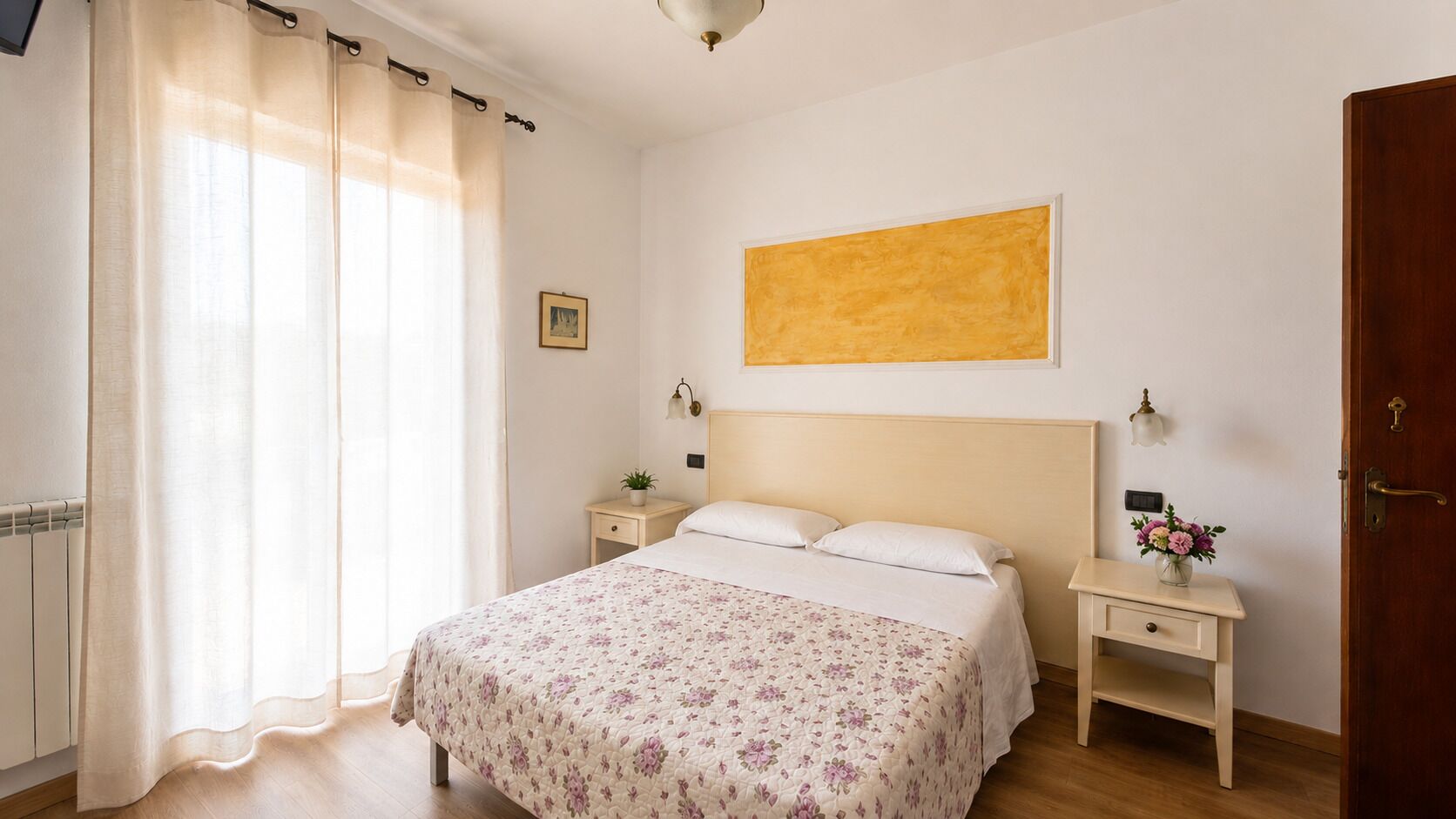 A bedroom with a bed, bedside tables, a nightstand, a painting, and a door.