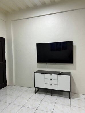 A room with a flat-screen TV mounted on the wall, a white cabinet with drawers, and a tiled floor. - Jaz Urban Stay - 337f (Angeles City)