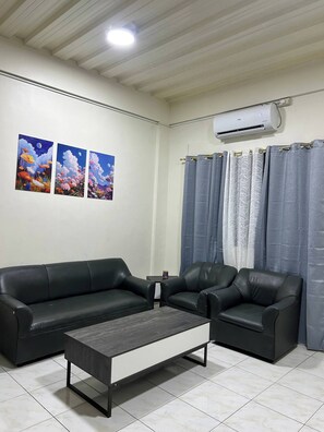 A living room with a black leather sofa, a coffee table, and a wall-mounted air conditioner. - Jaz Urban Stay - 337f (Angeles City)