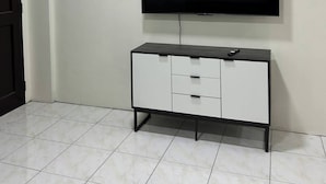 A room with a flat-screen TV mounted on the wall, a white cabinet with drawers, and a tiled floor. - Jaz Urban Stay - 337f (Angeles City)