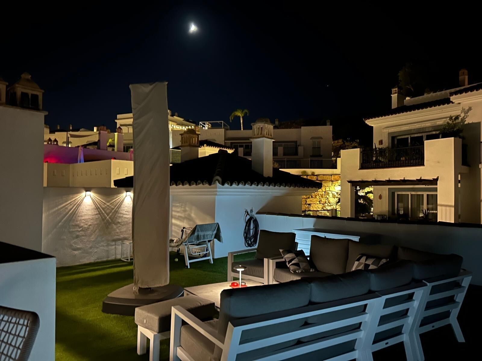 A nighttime outdoor seating area with a white sofa, a table, and a lamp.