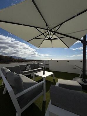 Terraza en la azotea con un sofá blanco para exteriores, una mesita y una sombrilla grande que proporciona sombra.