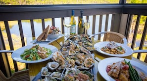 A dining table with various dishes, a bottle of wine, and a glass of white wine on a balcony overlooking a body of water. - Sea Clearly | Close to Beach | Golf Cart (LSV) | 4 Bikes | Pool (Santa Rosa Beach)