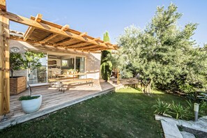 Una terraza de madera con mobiliario exterior, una pérgola y un césped bien cuidado.