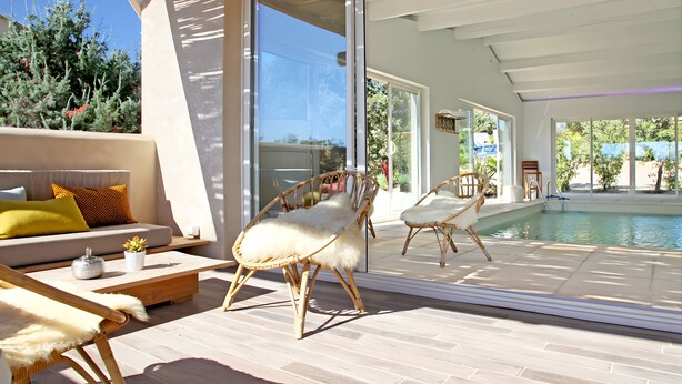 Un espacio exterior moderno con piscina, mobiliario de mimbre y un sofá con cojines.