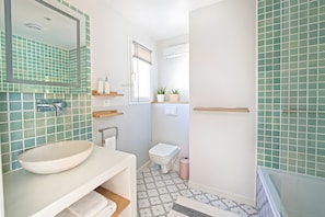 Un baño con lavamanos blanco, inodoro, espejo y ventana con persianas.