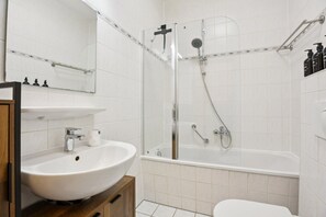 Moderni kylpyhuone, jossa on lasiseinällä varustettu suihku, valkoinen pesuallas ja wc.
