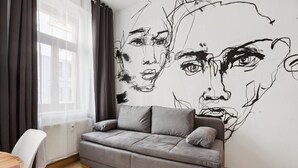 Un salón moderno con un sofá gris, una pared blanca con un cuadro abstracto negro, una mesa de comedor y un ventanal con cortinas.