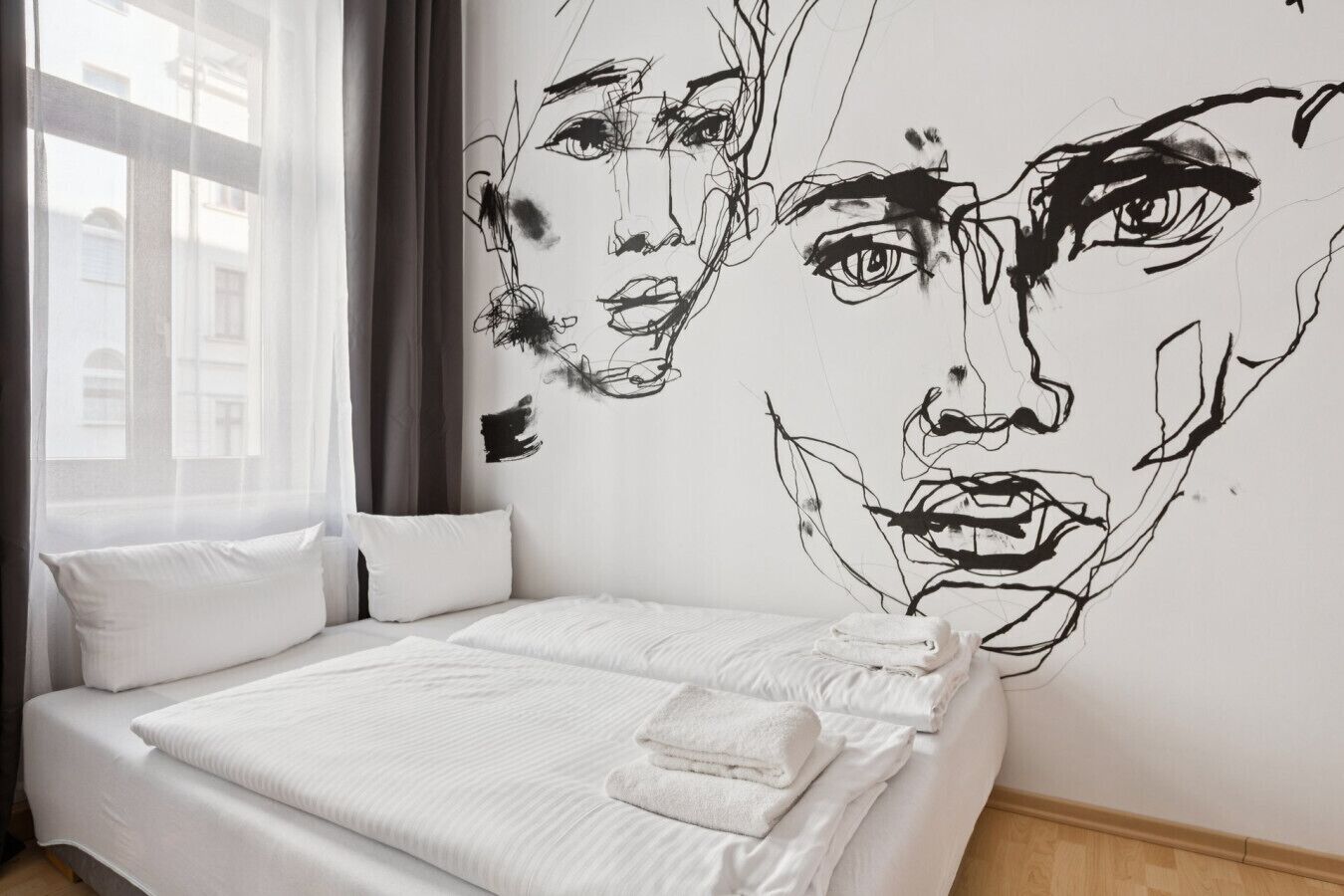 A bedroom with a large bed, white bedding, a window with curtains, and a wall mural.