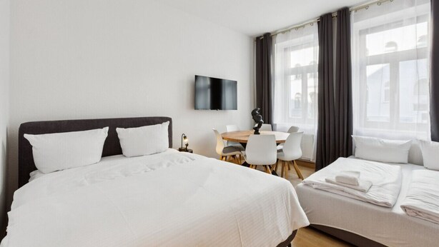 Habitación de hotel con dos camas, un escritorio, una silla, un televisor de pantalla plana y un ventanal con cortinas.
