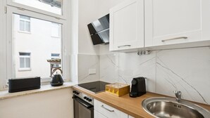 Una cocina con armarios blancos, un lavamanos de acero inoxidable, una estufa y una ventana con vistas a edificios.