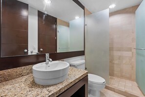 Un bany amb taulell de granat, un lavabo blanc, un vàter i una zona de dutxa.