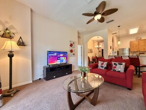 A living room with a TV, a glass coffee table, a red sofa, and a ceiling fan. - Disney Area 3BR Condo Pickleball, Pools & Free WiFi (Davenport)