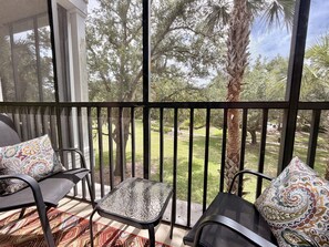 A balcony with two chairs and a small table, overlooking a garden with trees and a lawn. - Disney Area 3BR Condo Pickleball, Pools & Free WiFi (Davenport)
