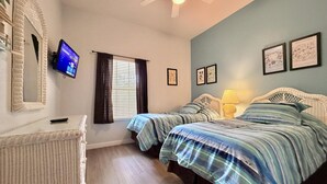 Un dormitorio con dos camas, televisión, ventilador de techo y obras de arte enmarcadas en las paredes.