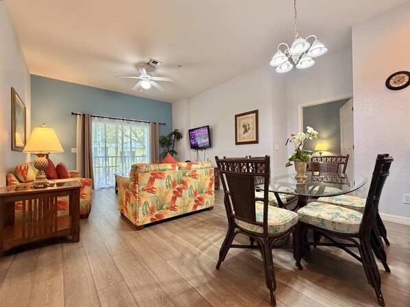 A living room with a sofa, a dining table with chairs, a ceiling fan, a TV, and a window with curtains. - Relax in Paradise! Spacious Bahama Bay Condo Near Disney (Davenport FL)