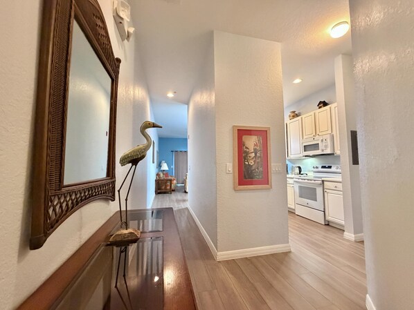 A hallway with a wooden floor, a mirror, a framed picture, and a kitchen area with white cabinets and appliances. - Relax in Paradise! Spacious Bahama Bay Condo Near Disney (Davenport FL)