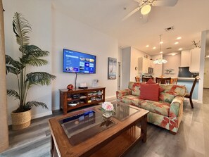 Ein Wohnzimmer mit Flachbildfernseher, Couch, Tisch, Bücherregal und einer Zimmerpflanze.