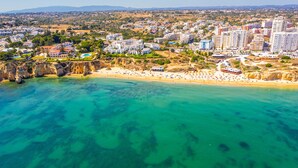An aerial view of a coastal town with a beach, clear turquoise waters, and residential buildings. - Villa Albert, Pool, Jacuzzi, Games Room (Armação de Pêra)