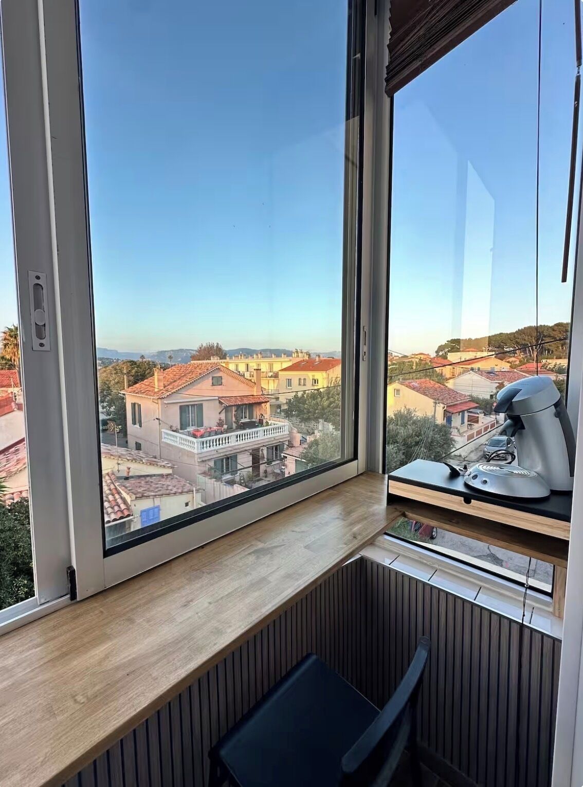 Una habitación con un ventanal grande, una cafetera en un estante y una silla.