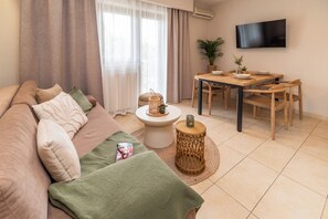 Uma sala de estar com sofá, mesa de jantar, cadeiras, televisão e janela com cortinas.