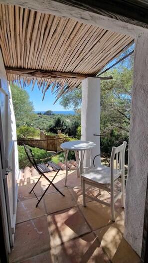 Um alpendre coberto com mesa e cadeiras, vista para a paisagem e uma parede de pedra.