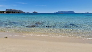 Une plage à l’eau claire, avec un rivage sablonneux et des montagnes qui se dessinent à l’horizon.