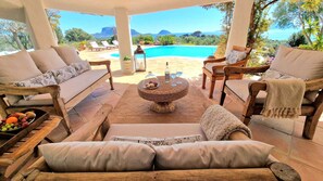 A covered outdoor seating area with a pool, lounge chairs, and a wicker coffee table. - Villa Cala Sassari - A refined Sardinian villa for families and groups (Sassari)