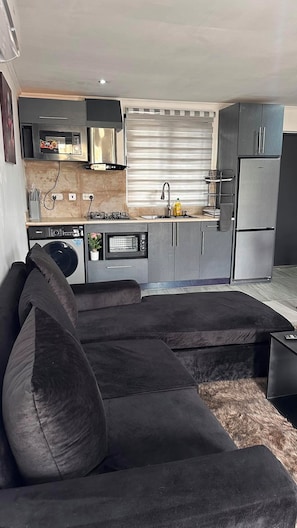 Eine moderne Küche mit Einbauofen, Mikrowelle und Kühlschrank. Es gibt einen Essbereich mit einer Couch und einem kleinen Tisch.
