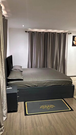 Ein Schlafzimmer mit Bett, Nachttisch, Schublade, Wandregal und Vorhang.