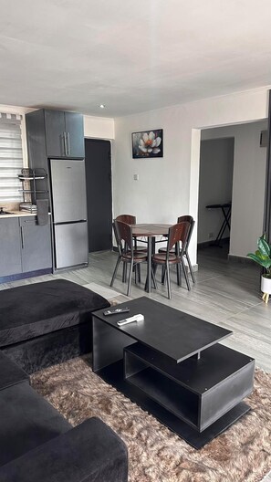 Ein modernes Wohnzimmer mit einer schwarzen Couch, einem Couchtisch und einem Essbereich mit vier Stühlen.