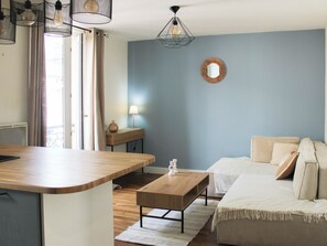 Un salon moderne avec une table basse en bois, un canapé, une table d’appoint avec une lampe et un miroir fixé au mur.