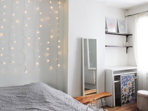 Une chambre à coucher avec un lit, un bureau, une chaise, un miroir et des guirlandes lumineuses.