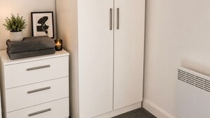 Ein weißer Kleiderschrank mit zwei Türen und ein kleiner Nachttisch mit Schubladen.