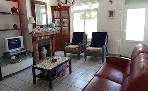 Ein Wohnzimmer mit Fernseher, Kamin, zwei Sesseln, einer Couch und einem Couchtisch.