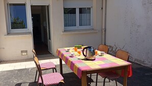 Un espacio exterior para comer con una mesa para dos, sillas y una ventana con persianas.