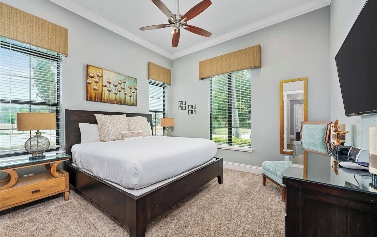 A bedroom with a bed, bedside tables, a ceiling fan, a desk, and a TV.
