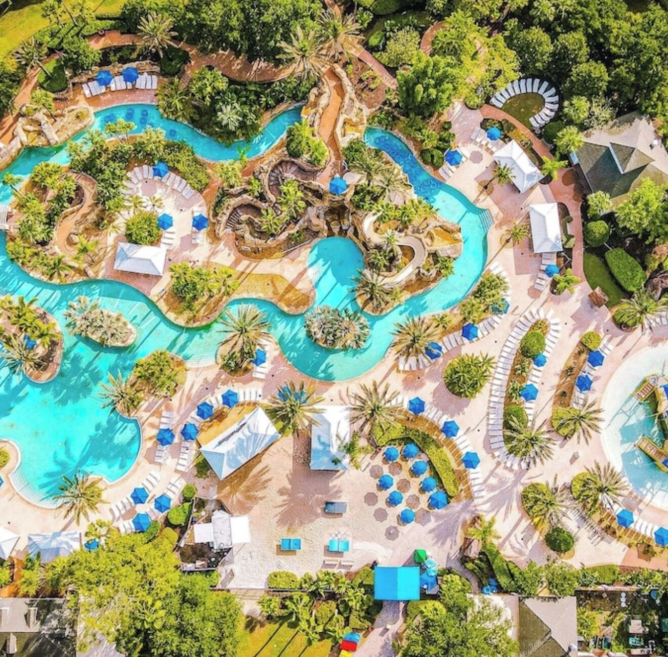 An aerial view of a resort with multiple swimming pools, lounge areas, and tropical landscaping.