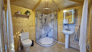 Un baño de cabaña de madera con ducha envuelta en vidrio, inodoro, lavamanos y espejo.