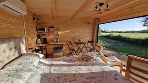 Una cabaña de madera acogedora con una cama, un kitchenette y una mesa con sillas.