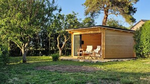 Une cabane en bois avec une porte en verre, deux chaises et une table à l’extérieur.