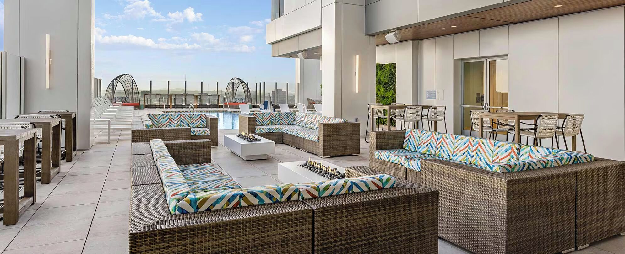 Un área de lounge en la azotea con muebles de mimbre, piscina y bar.