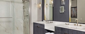 A modern bathroom with a glass shower enclosure, two sinks with gold faucets, and pendant lighting. - Resort in Centennial Park District of ATL, 2 bedroom presidential reserve suite (Atlanta)