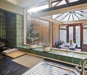 A kitchen with a window, a sink, a countertop, and a dining area with a table and chairs. - 4BR Family Home with Jacuzzi Near Birmingham (West Midlands)