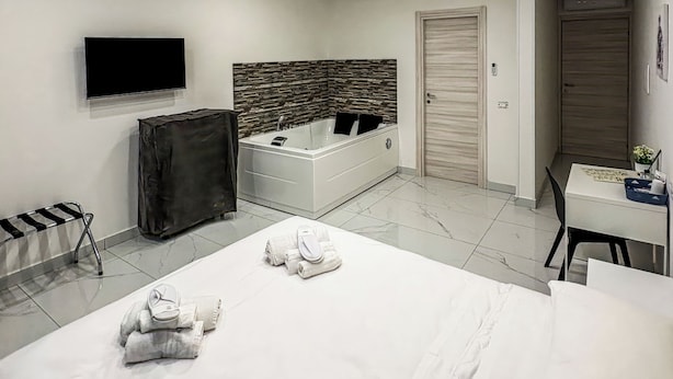 Una habitación de hotel moderna con una cama grande, un televisor de pantalla plana, un escritorio pequeño y una zona de ducha.
