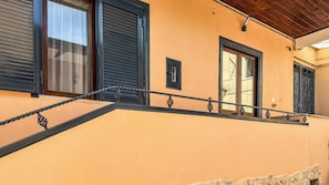 Un edificio con balcón, ventana con reja de metal y puerta con marco negro.