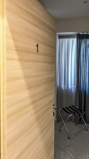 Una habitación moderna con una puerta de madera marcada con el número 1, una silla de metal y una ventana con cortinas de gasa.